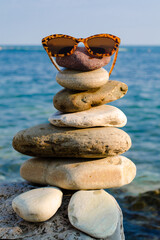 sea stones are stacked in the form of a human figure with glasses on the background of the blue sea.Vacation on the ocean coast.Sea, sun and water on the beach.