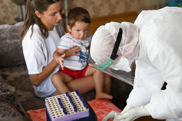 a doctor in a protective suit takes a blood test from a child at home