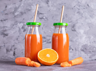 Carrot and orange juice in glass bottles with eco straws on a light background