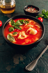 Tomato soup with tortellini in black bowl on dark background. Selective focus. Tomato soup with tortellini in black bowl on dark background. Selective focus. Top view. Vertical photo