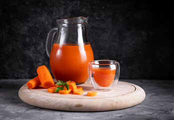 Carrot and orange juice in a jug on a wooden round board in low key