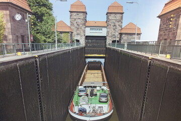 Langes Containerschiff in Schleuse mit zwei steinernen Türmen im Hintergrund. Das Boot ist noch unten und wartet darauf nach oben gefahren zu werden Zwei Autos und ein Fahrrad an Deck Donau Bratislava