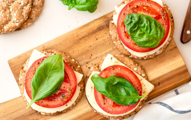 Crispbread with cheese, tomato and basil leaf on a light background top view. Tasty diet snack or breakfast. Vegetarian food.