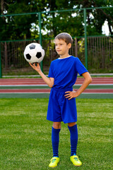 a small football player with a ball stands on a green football field.