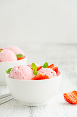 Strawberry ice cream in a bowl with fresh strawberries and mint on a wooden background. Copy space.
