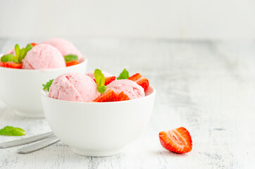 Strawberry ice cream in a bowl with fresh strawberries and mint on a wooden background. Copy space.