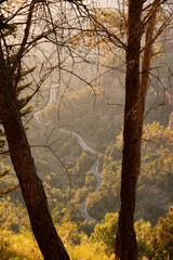A car drives up windy road leads up forest mountainside up the Catalan town of Siurana. This impressive plateau is on top of red dramatic cliffs. Beautiful sunset, golden hour light.