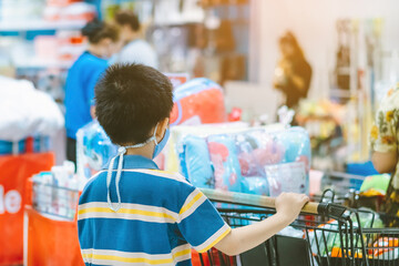 Back view of boy wearing face mask to prevent the spread of the Corona Virus (Covid-19) shopping in a supermarket. Boy with shopping cart during virus outbreak in grocery store. New normal lifestyle.