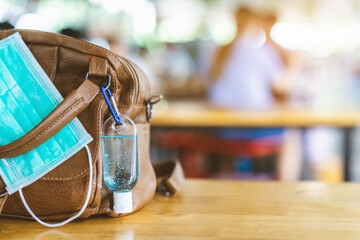 Mini portable alcohol gel bottle to kill Corona Virus(Covid-19) hang on a leather shoulder bag of a woman with a surgical mask on table at cafeteria.New normal lifestyle.Selective focus on alcohol gel