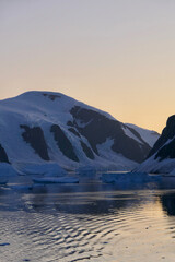 Fototapeta na wymiar Antarctica, sunset orange evening sky, water reflection with ice and mountains