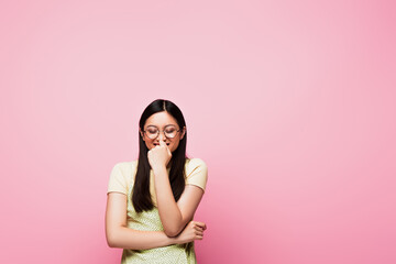 Fototapeta premium cheerful and young asian woman with closed eyes touching glasses isolated on pink