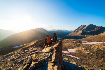 Couple of hikers looking at view from mountain top against sun burst. Man and woman on vacation in scenic alpine landscape, summer activities fitness wellbeing freedom