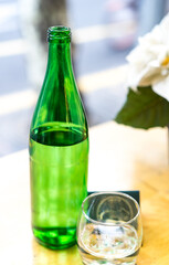 Mineral water in a green glass bottle with a glass on the wooden table at the restaurant, welcome drink, selective focus, beautiful blurred bokeh, bottle of water