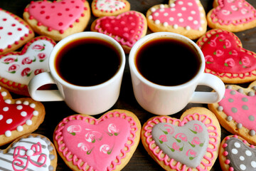 Closeup two cups of hot coffee among heap of homemade heart shaped royal icing cute patterned cookies