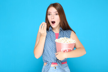 Surprised girl with bucket of popcorn on blue background