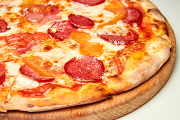 Pizza with salami, bell pepper, tomatoes and cheese on a light background. Close-up, selective focus