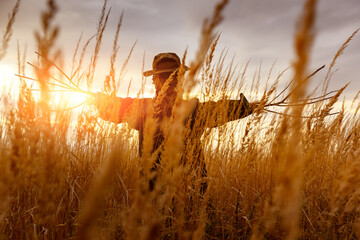 Terrible scarecrow in dark cloak and dirty hat stands alone in a autumn field at sunset time....