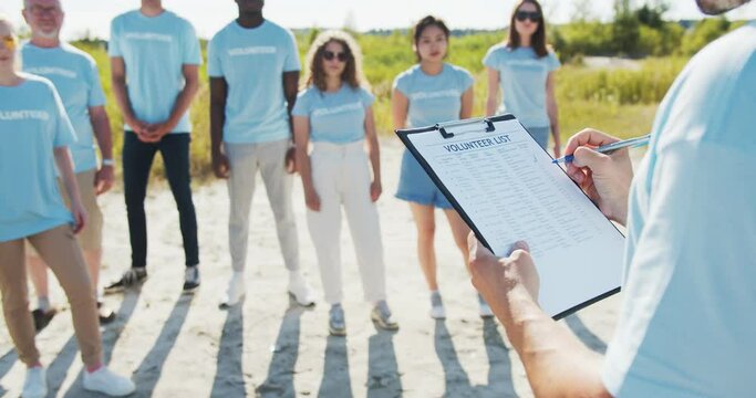 Close up of a clipboard with the volunteer list. The leader dividing responsibilities and checking the presence of members, participants. Nature and environment conservation concept. Save ecology.