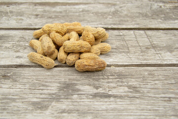On a wooden table are unpeeled peanuts. A small slide of useful and delicious earthen nut