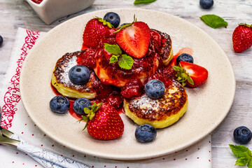 Cottage cheese pancakes with fresh berries and strawberry sauce. Healthy breakfast concept on wooden background
