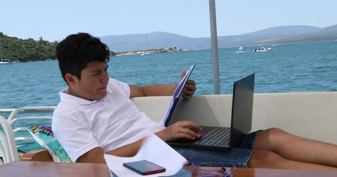 Teenage boy studying on yacht deck Online learning education distance learning for kids at home Homeschooling during quarantine or isolation