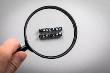 Swedish Economy. Man's hand, holding magnifying glass. Imports and Exports, Growth, Planning and...