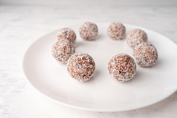 A white plate with round sweets made of dates and coconut shavings on a light wooden background