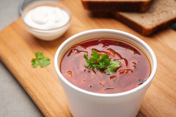 Borscht decorated with greens in a disposable dish next to sour cream and bread