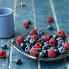 Food background. Ethno plate with blueberries, raspberries. Lavender on a blue background.