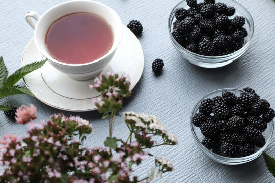 A Cup of herbal tea with medicinal herbs and blackberries in a glass container on a gray background, side view, bokeh