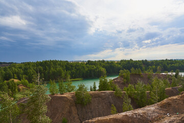 Green lake among the sand hills on the textured background of the cloudy sky.