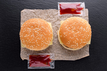 top view of two tasty homemade burgers on paper and ketchup on black background