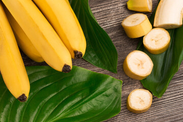 Bunch of raw organic yellow bananas with slices and green leaves on wooden background - 369313889