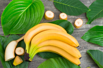 Bunch of raw organic yellow bananas with slices and green leaves on wooden background - 369314065