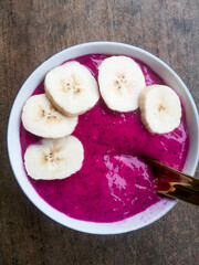 Dragon fruit smoothie bowl with sliced banana isolated on white bowl and ceramic golden color spoon.