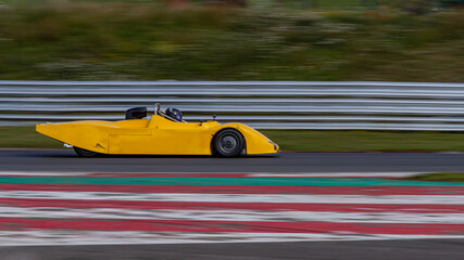 A panning shot of a yellow racing car as it circuits a track.