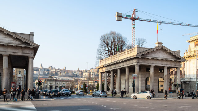 BERGAMO, ITALY - FEBRUARY 19, 2019: people and cars near old medieval propylea of Porta Nuova on street Largo Gianandrea Gavazzeni in Lower Town (Citta Bassa) of Bergamo city