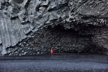 Iceland tourist woman walking on Reynisfjara black sand beach by basalt columns and cave, beach of...