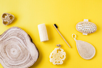 Frame from loofah sponges, massager, toothbrush, wooden comb, wood slice on yellow surface. Collection for bath from ecological material. Zero waste for bath. Copy space, flat lay.