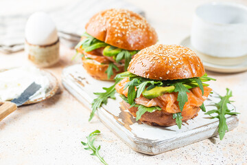 Burger sandwich with salmon, cream cheese, avocado and arugula on a light background, concept diet food, sandwich take away, healthy fast food