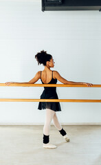 Back view of young female ballet dancer resting at barre in studio
