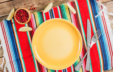 Festive Mexican table setting. Plate and cutlery with colorful napkin on rustic wooden background....