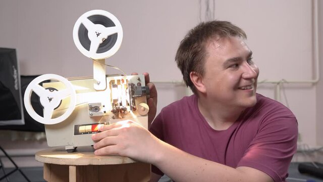 Young man tries to turn on old vintage reel film projector to arrange traditional old school movie screening at home with friends or family. Light comes on and guy smiles triumphantly.