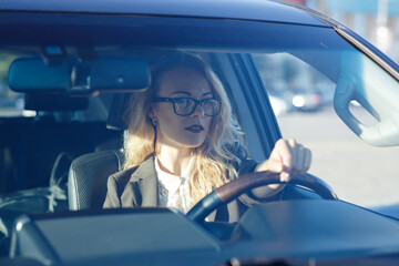 Beautiful young woman with blond curly hair wearing a suit  and glasses in  a car 