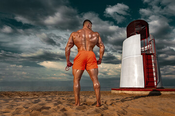 Fit athlete bodybuilder on the beach. Attractive young man lifeguard near the observation tower on the beach.