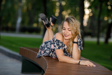 Beautiful young woman with blond curly hair wearing a dress and glasses lying in a park