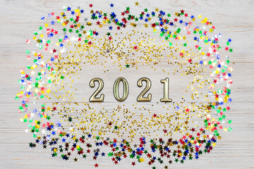Golden numbers 2021 surrounded by gold and colored stars on a light wooden background. The symbol of the new year. New Years Celebration 2021.