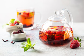 Fruit red tea with berries in glass teapot on white background