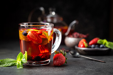 Fruit red tea with berries in glass cup on black background