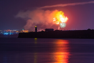 Festive salute over the city of Sevastopol on the day of the Navy. Bright multicolored flashes of fireworks. The concept of the celebration. Night shooting of the city. Silhouette of the lighthouse.